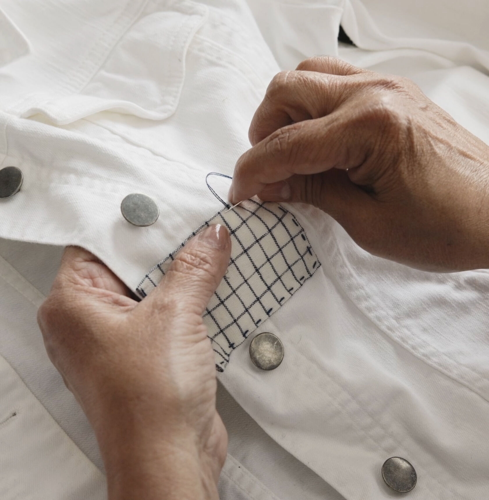 Hands making final stitches on a rectangular fabric patch.