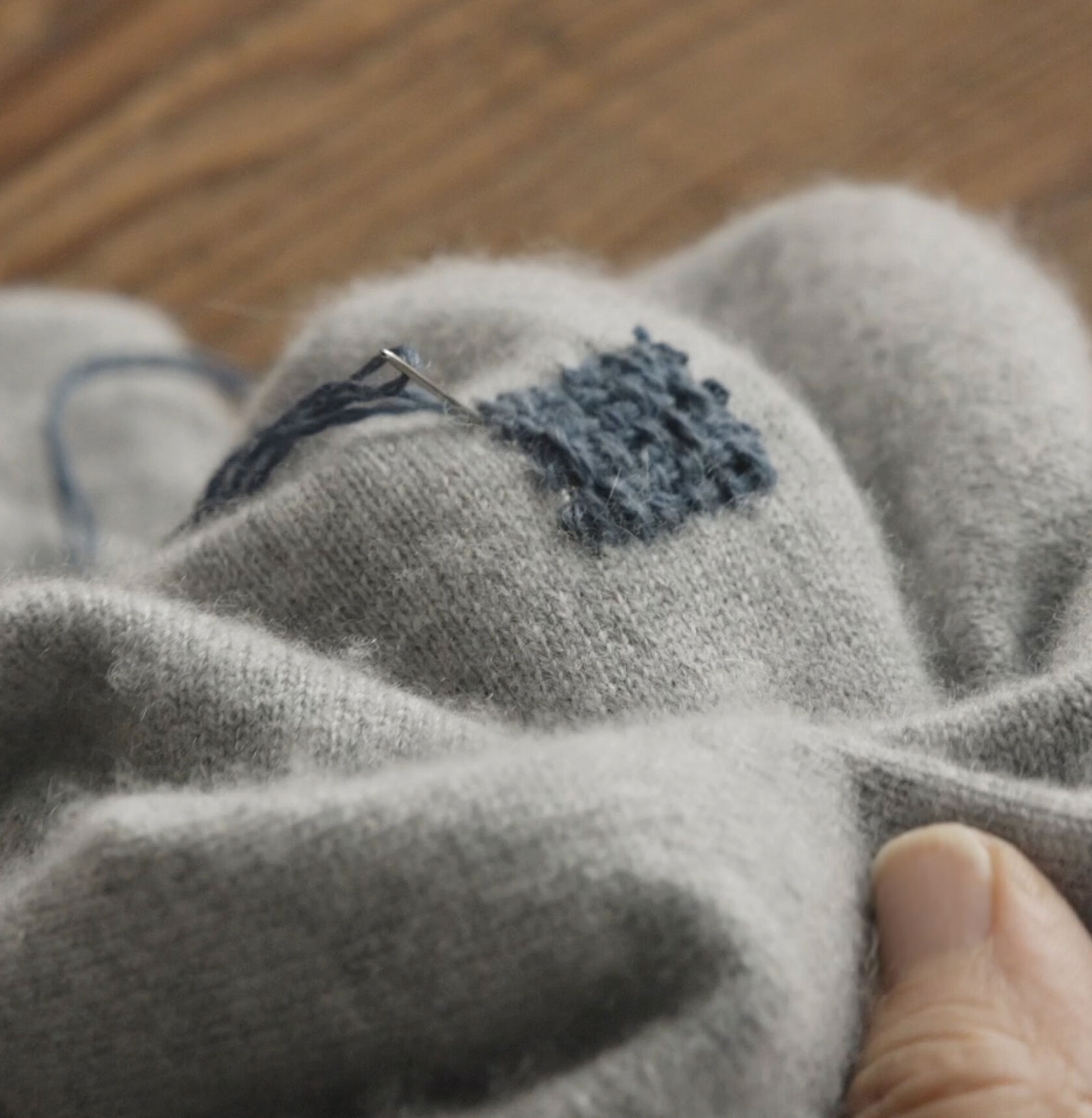 Making final stitches on blue embroidery square. 