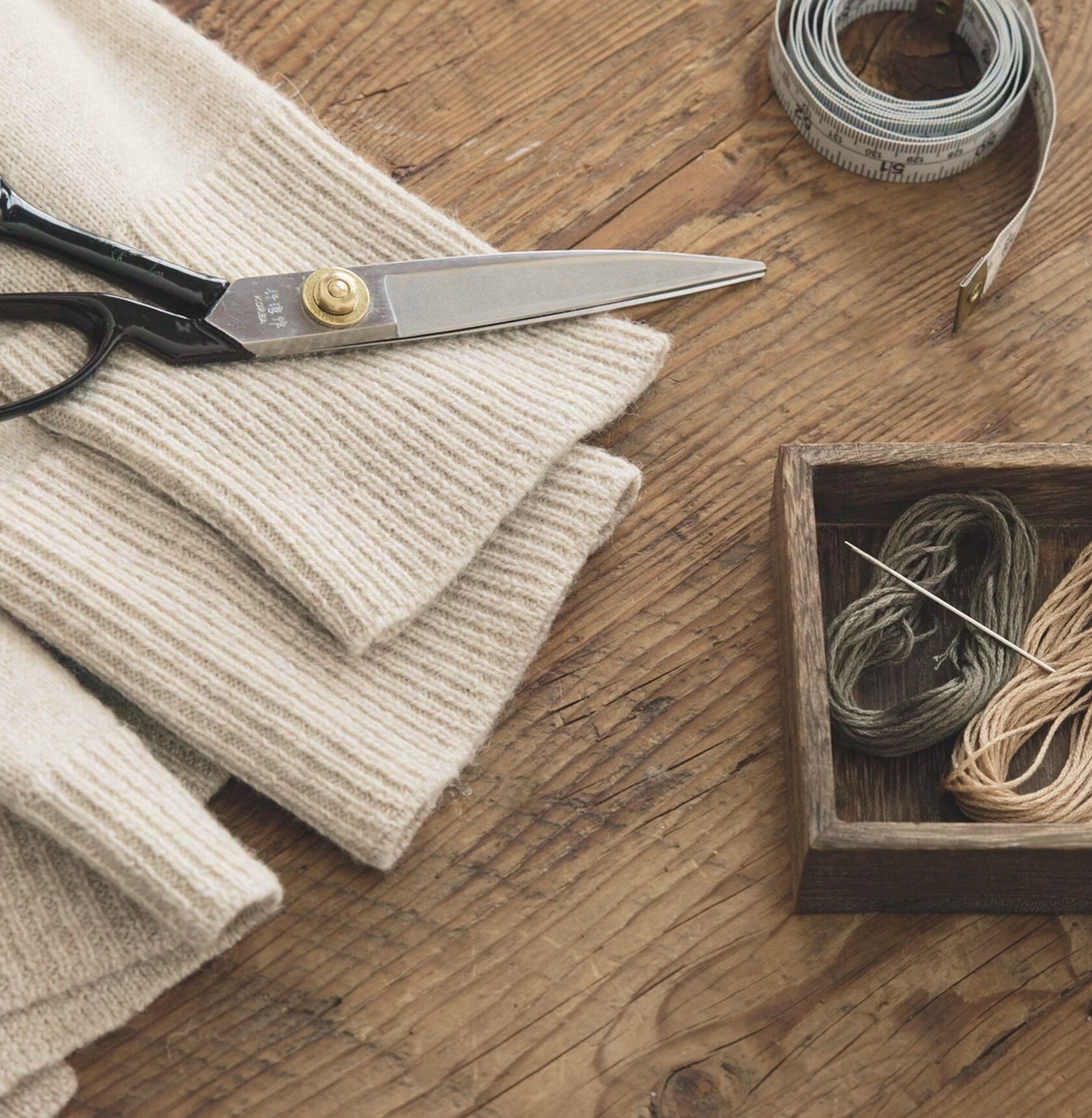 Scissors, a needle, thread and a sweater on a table.