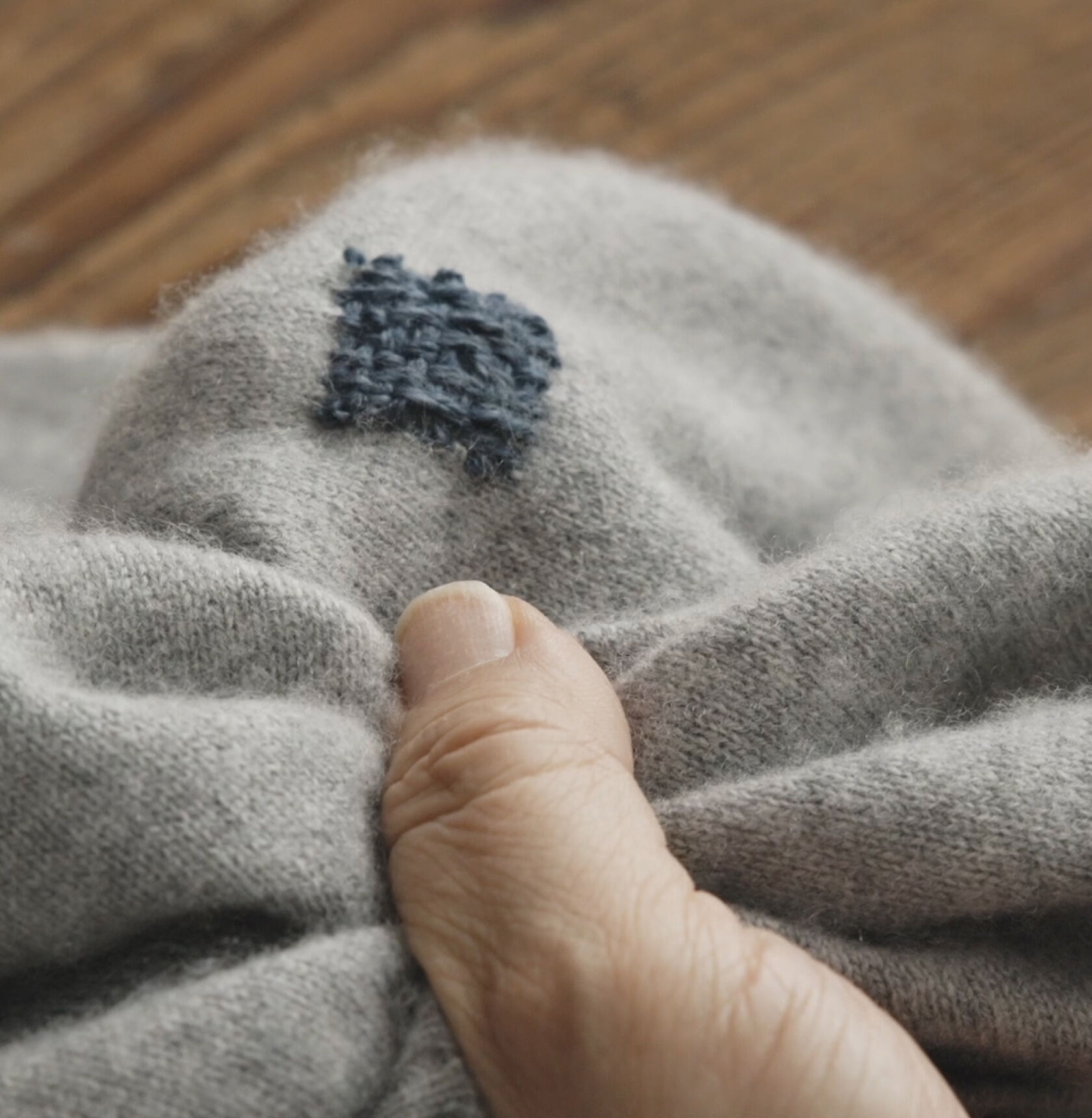 Close-up of a blue embroidered square on a mended gray sweater.