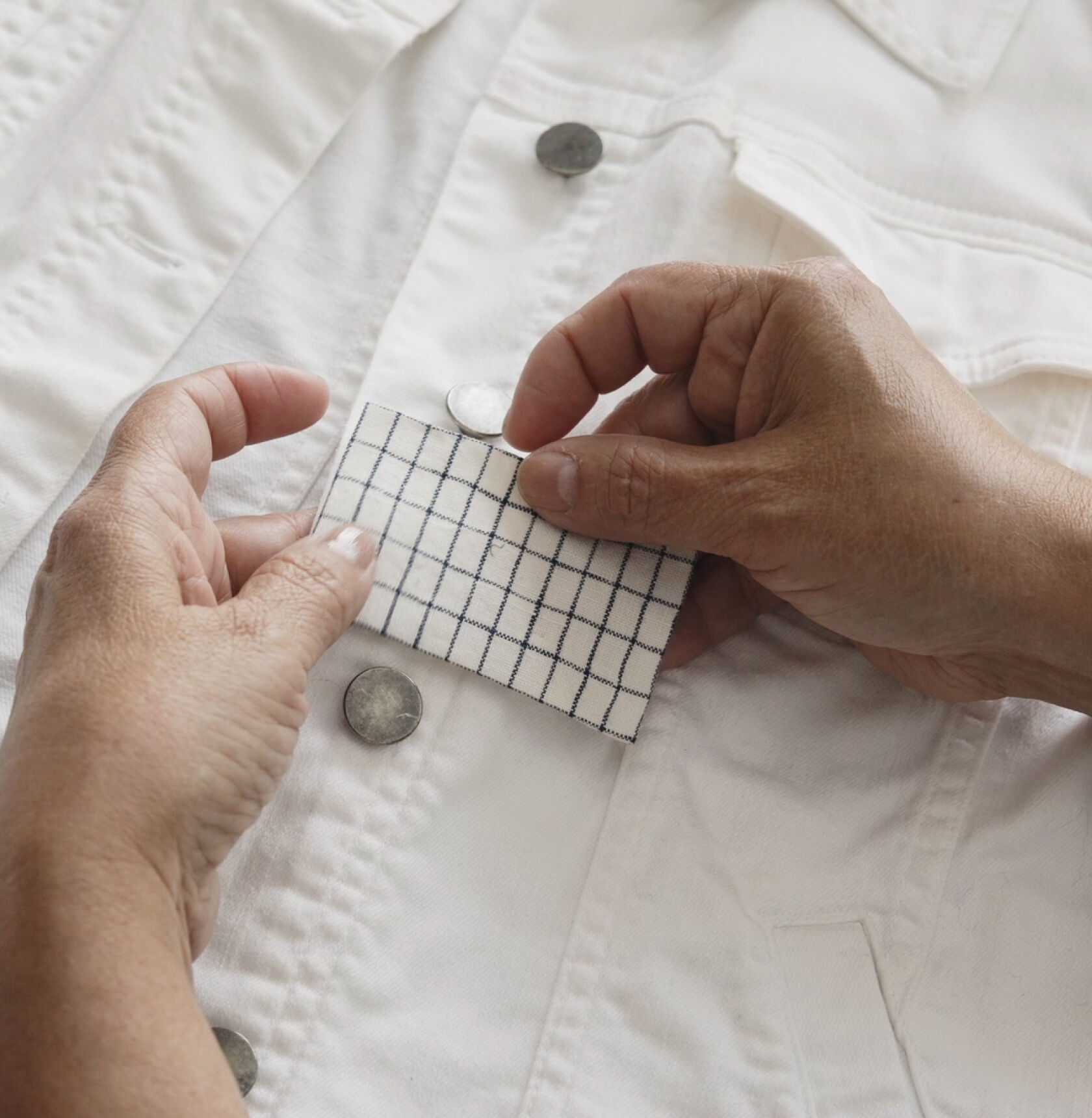 Hands holding a fabric patch against white denim jacket.