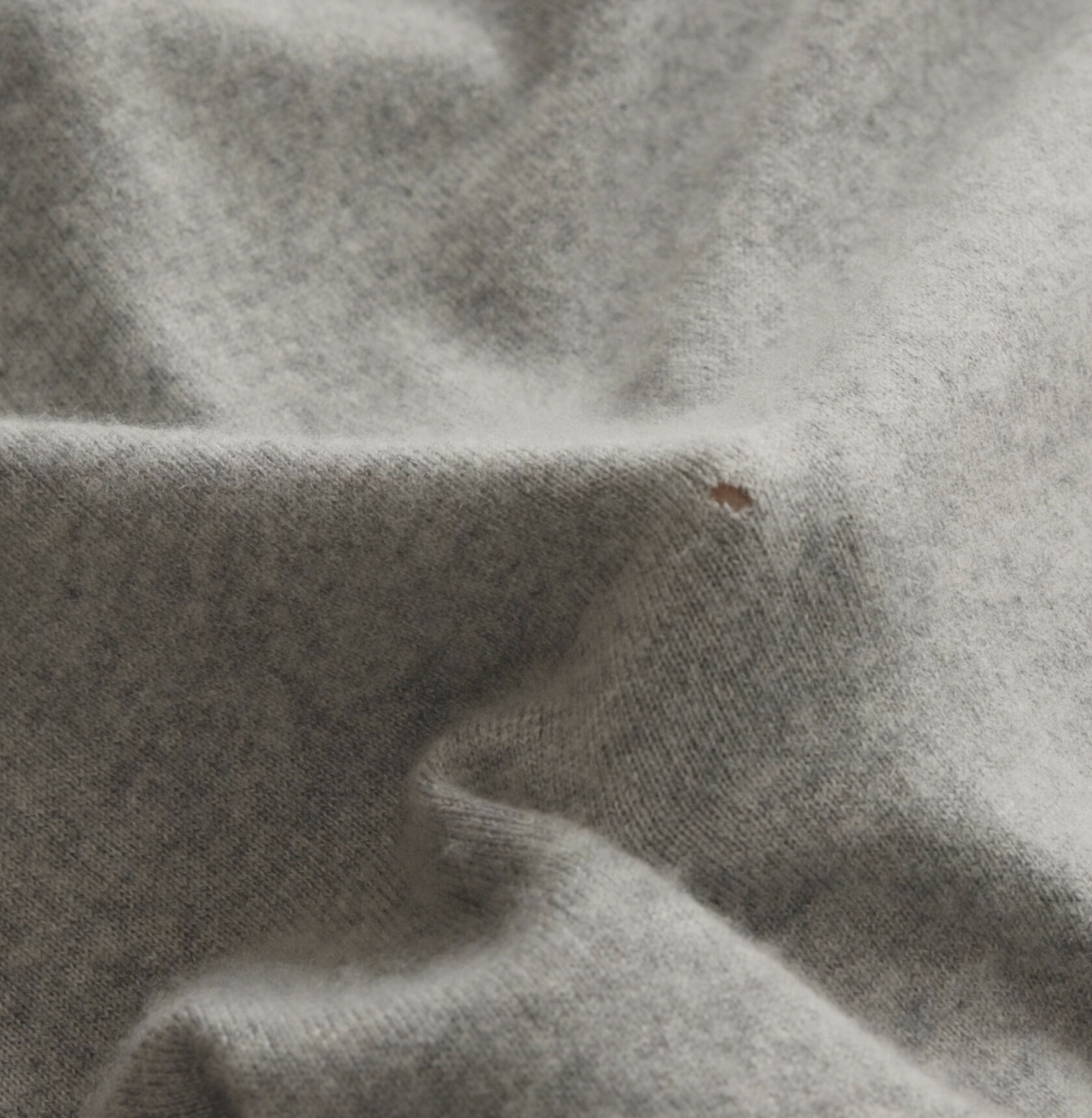 A gray sweater with a small moth hole. 