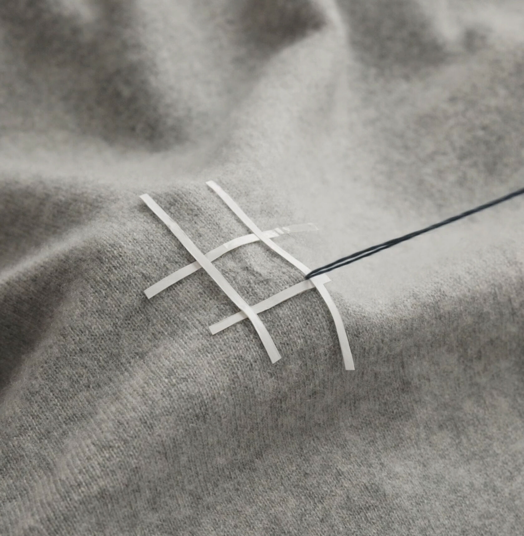 Close-up of hands stitching with a blue thread on a gray sweater.