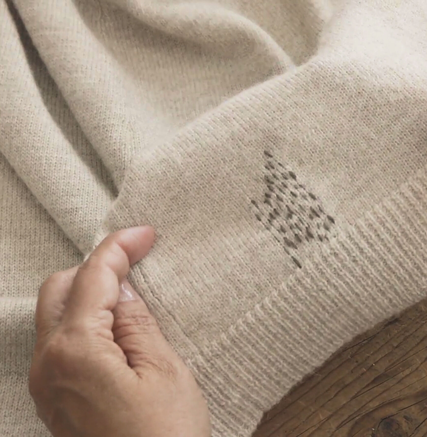 Completed visibly mended running stitch pattern on a beige sweater.