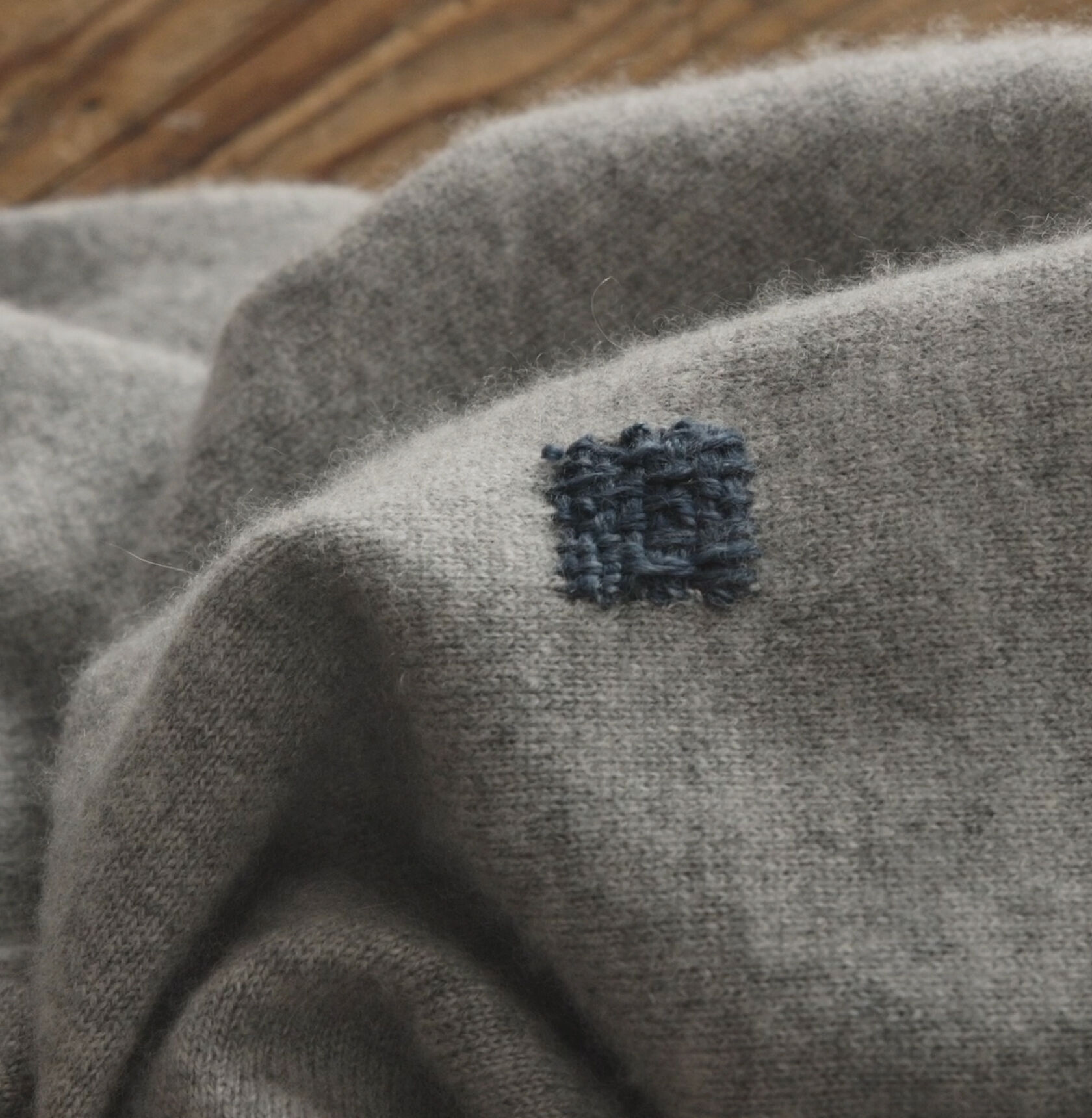 Completed blue thread visible repair square on gray sweater.