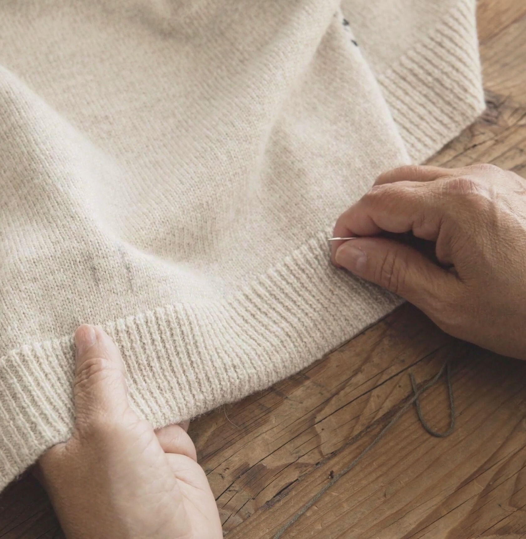 Hands holding a needle and a beige knit sweater with a slight flaw on it.