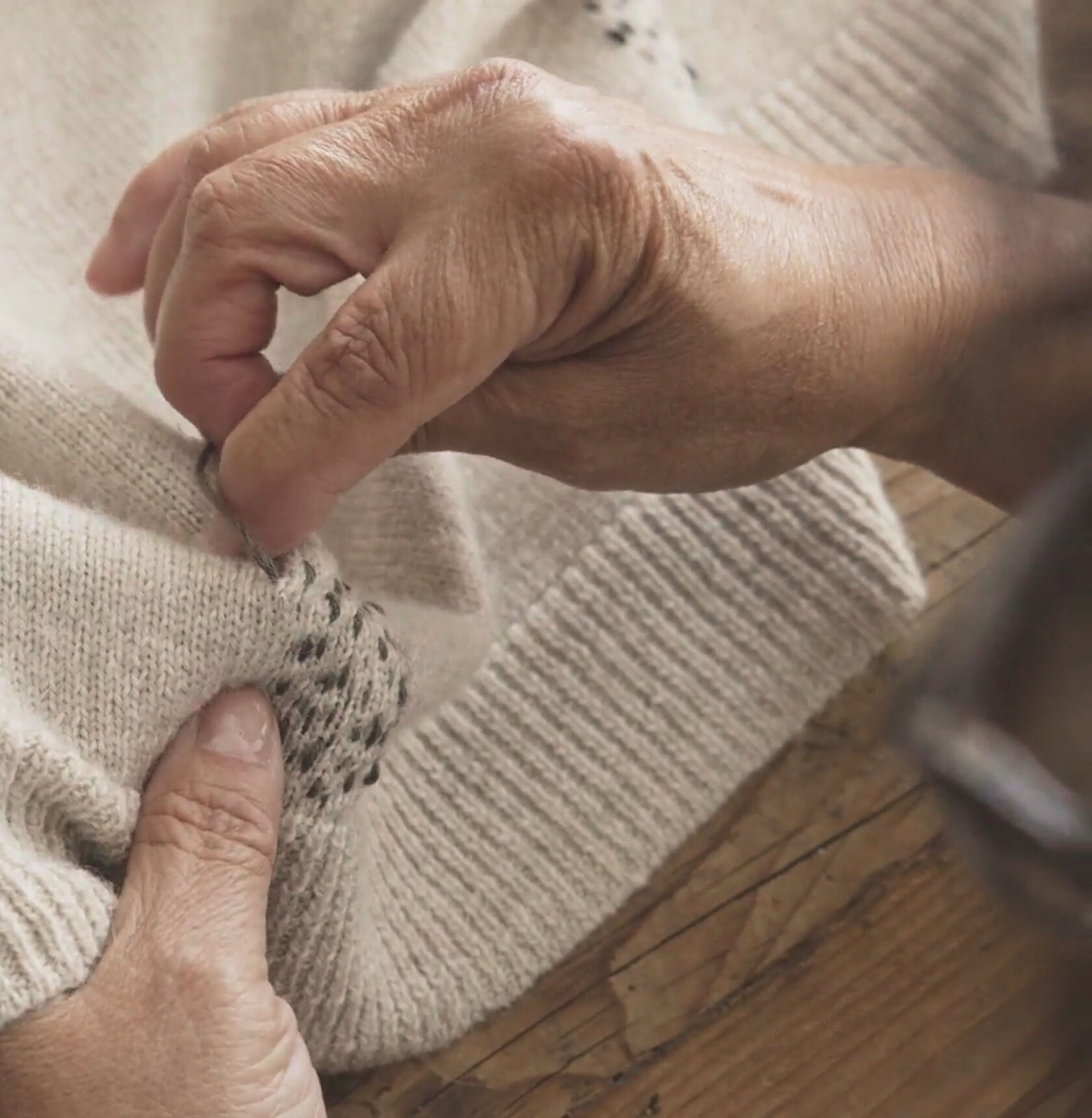 Hands creating a stitching pattern using contrasting thread on a beige sweater.