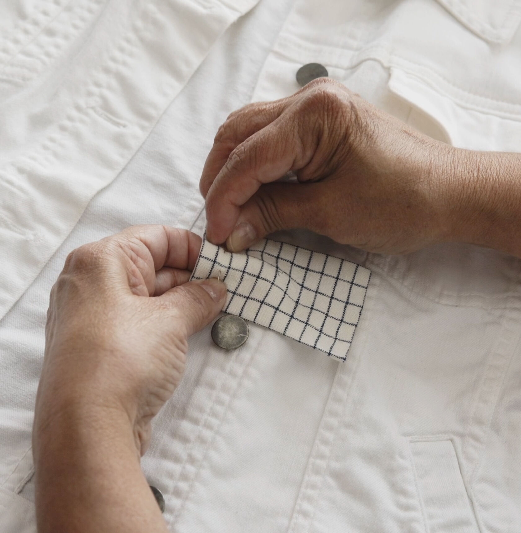 Hands pinning a fabric patch on white denim jacket.