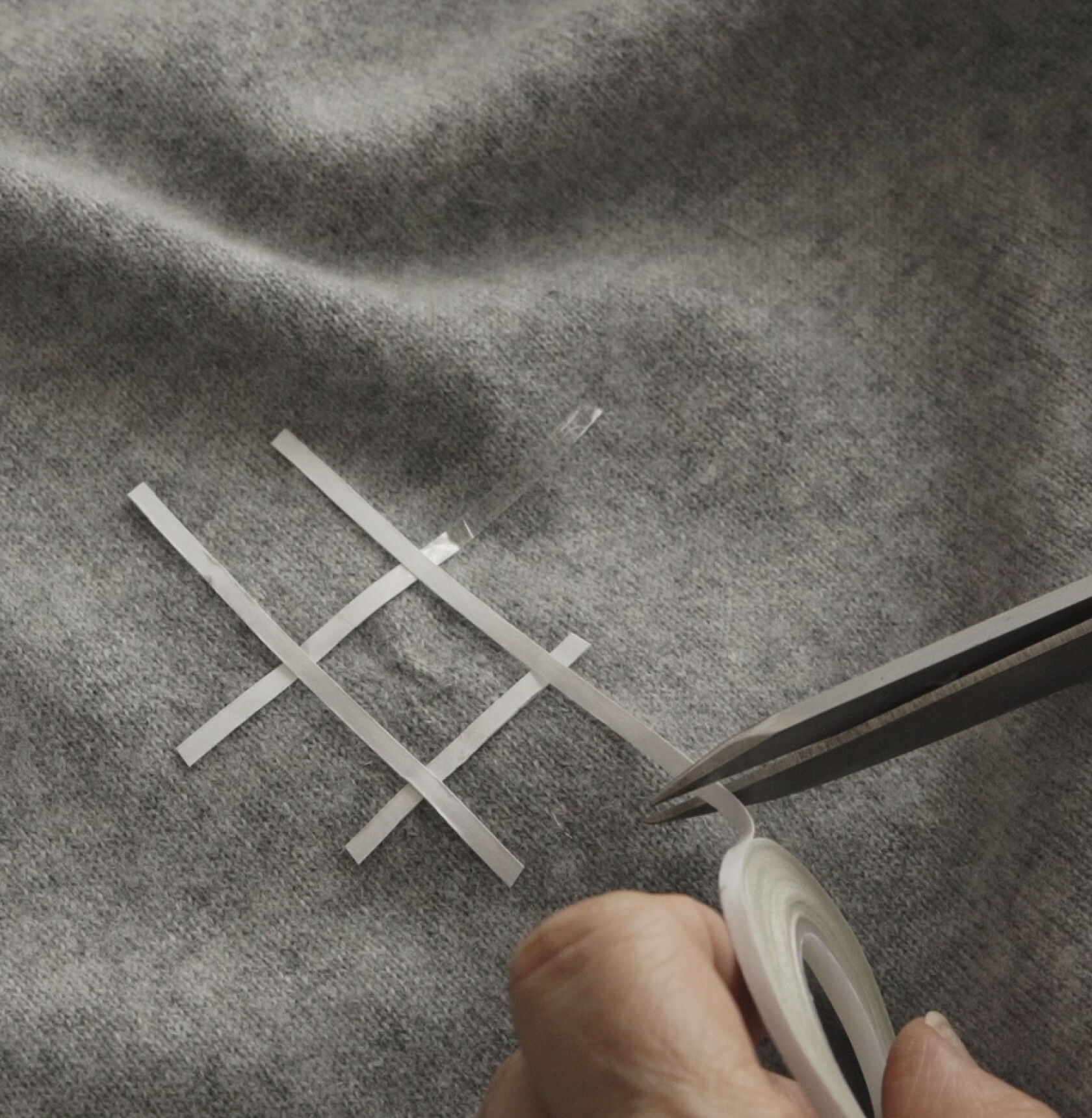 Close-up of hands taping a small square on a gray sweater.