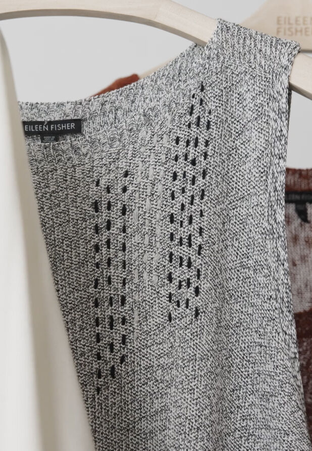 A damaged EILEEN FISHER garment that has been visibly mended with contrasting thread.