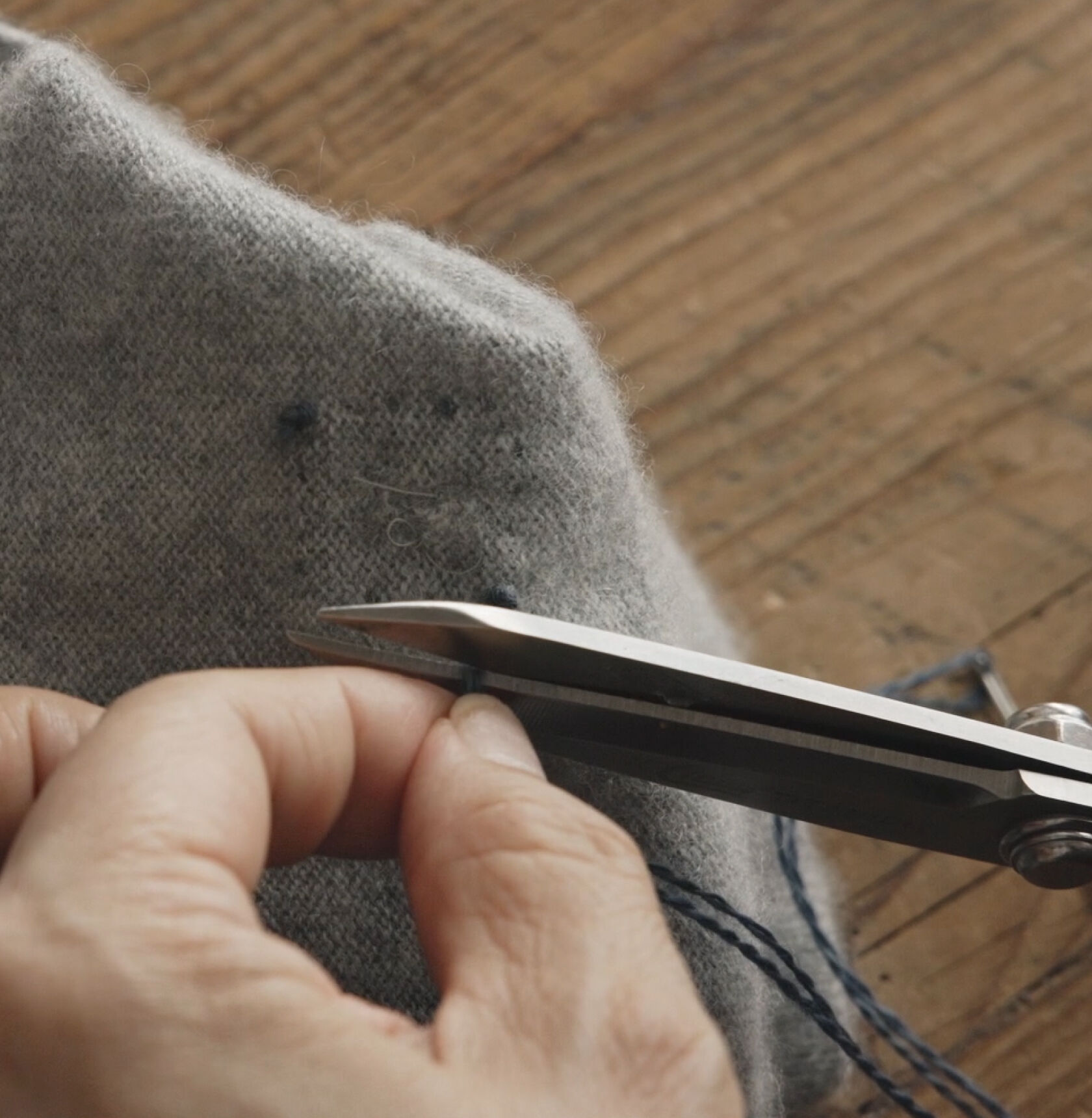 Tying off blue thread on a mended gray sweater. 