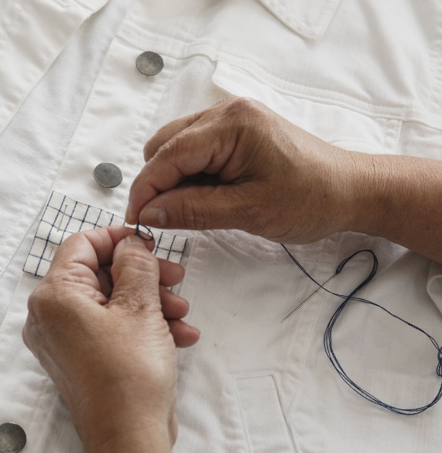 Hands threading a needle with blue thread.